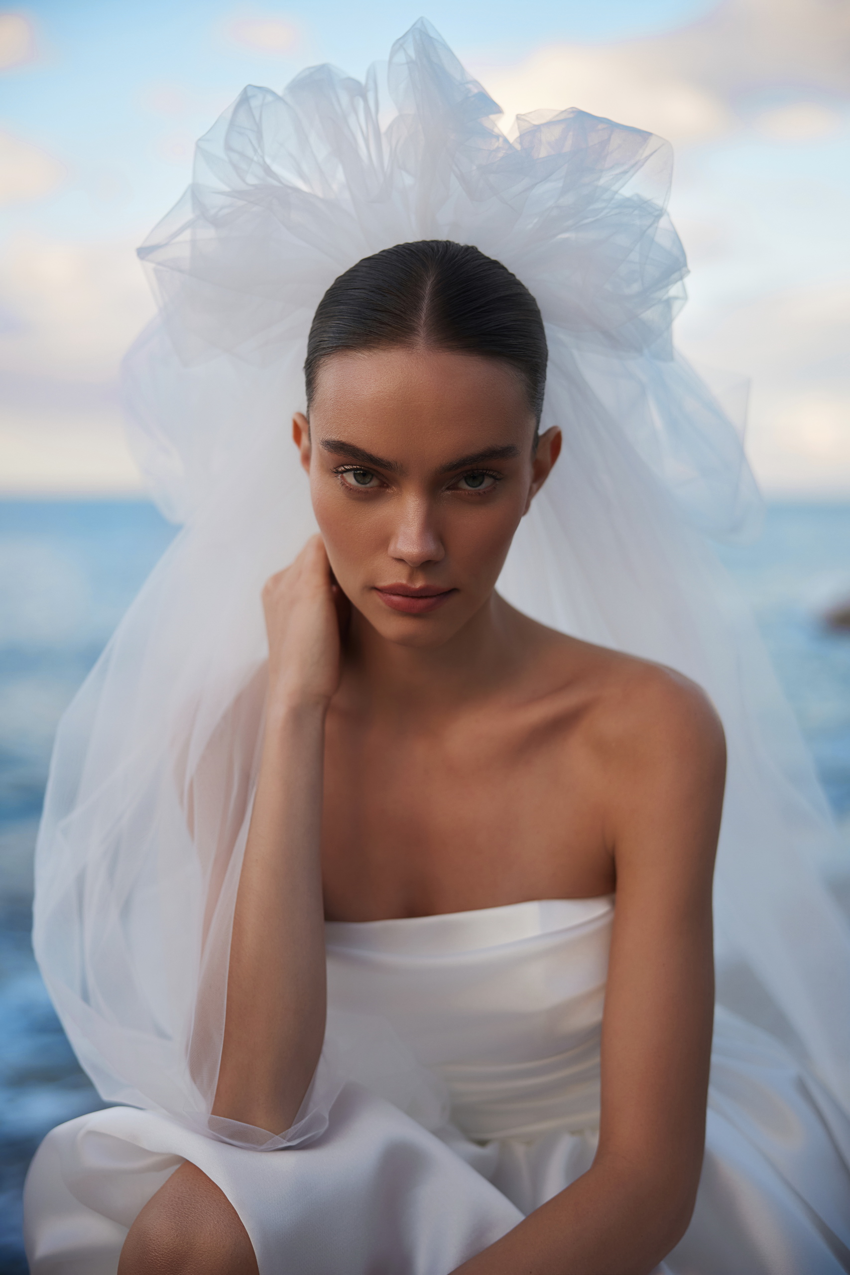 Bride in a lace wedding dress with a deep V-neck against a blue sky.